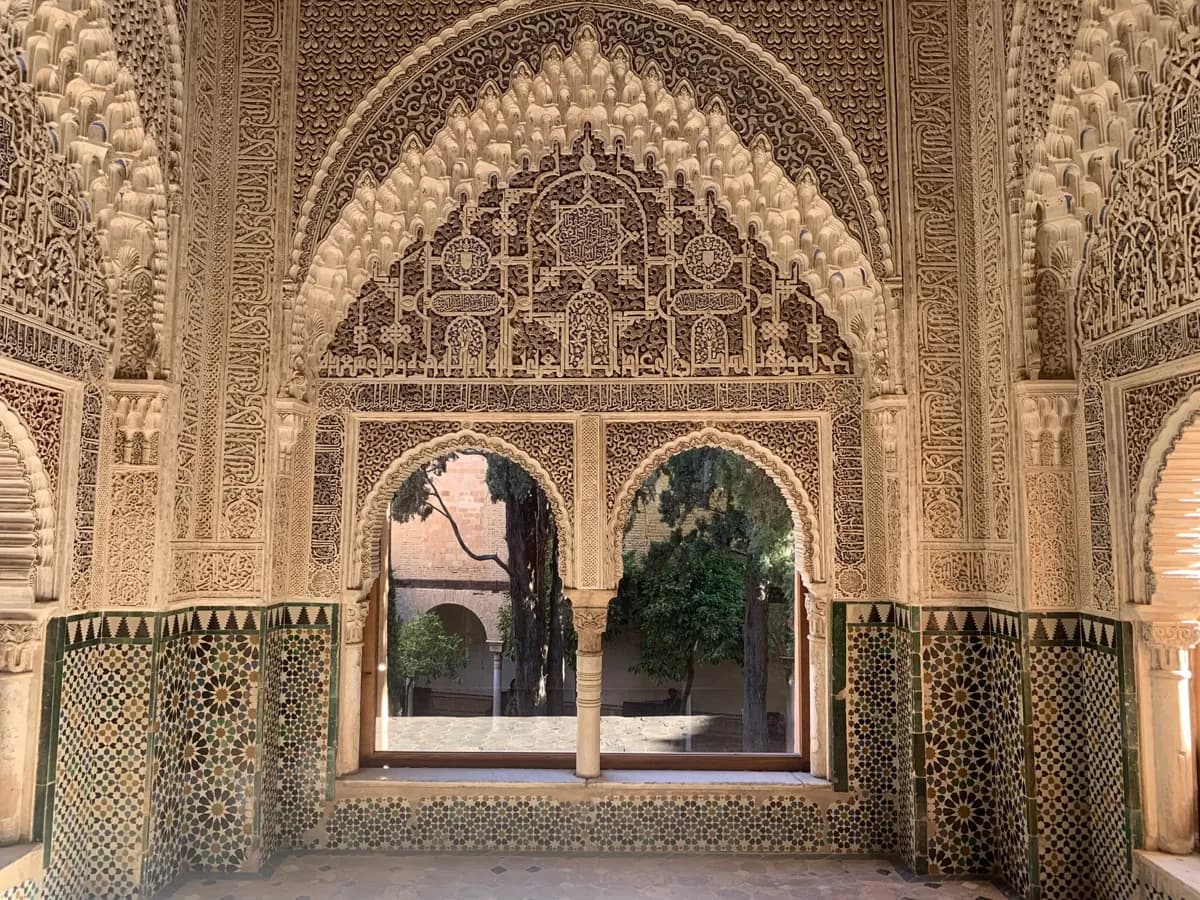 Carved arches and a window looking out from a hall of the Alhambra
